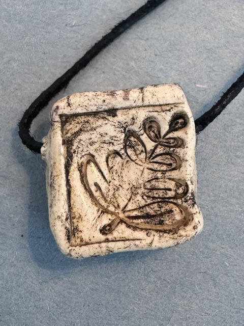 Handmade ceramic pendant stamped with a leaf symbol, worn on a cord